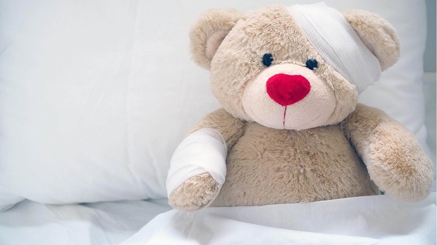 Erste Hilfe bei Kindern: Ein Teddybär ist im Bett und hat einen Verband um seinen Kopf. Erste Hilfe bei Kindern: Ein Teddybär ist im Bett und hat einen Verband um seinen Kopf.